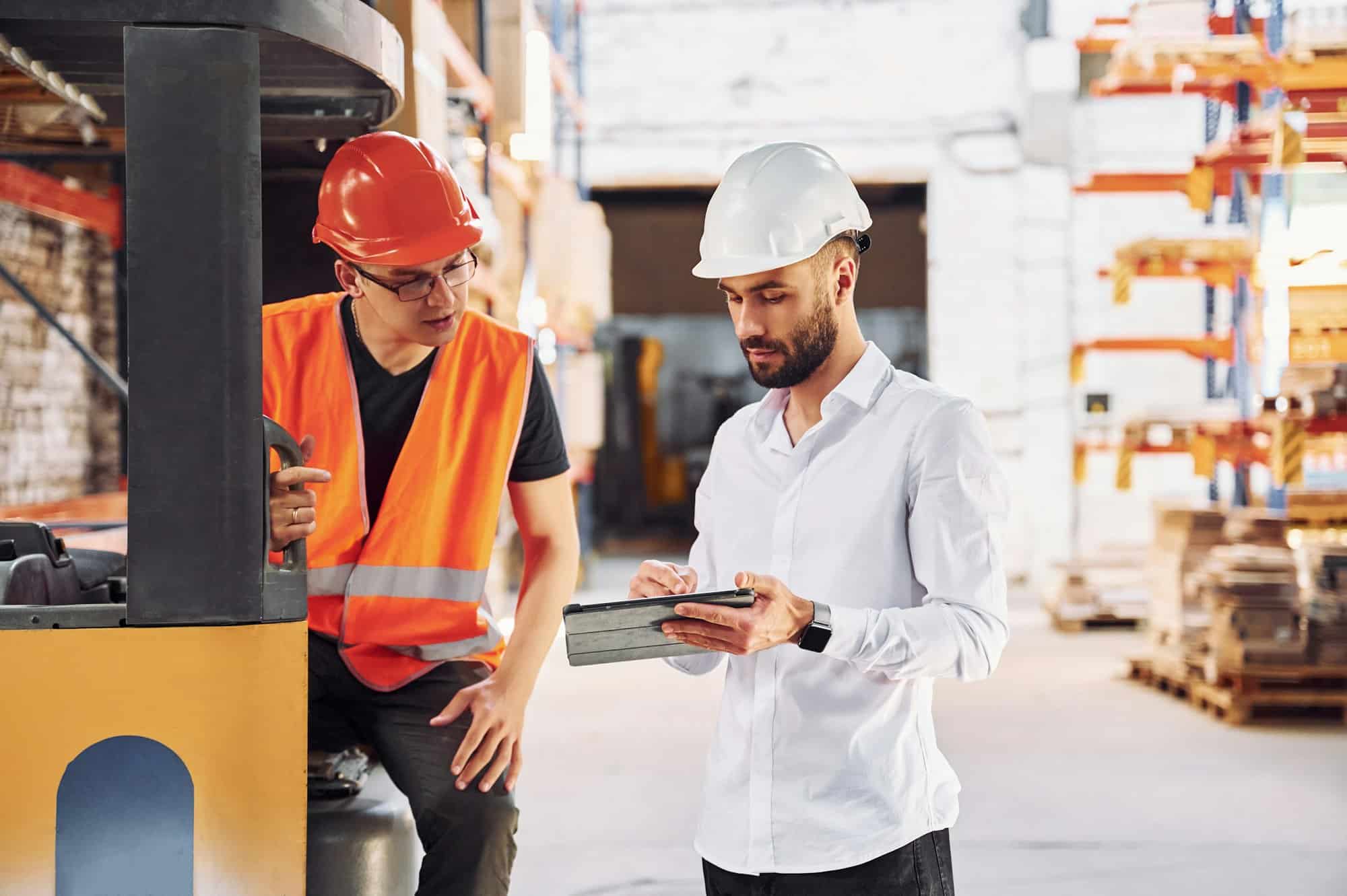 With tablet and cargo moving transport. Two storage workers is in the warehouse